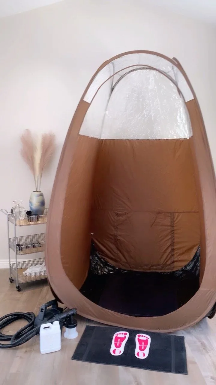 Carpa profesional de bronceado montada en una sala, con el equipo de aerógrafo y tapete listos